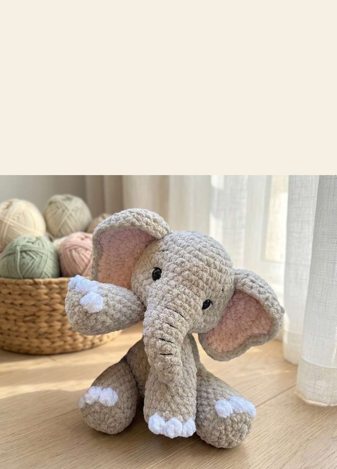 Pebble the Elephant, a crocheted amigurumi, beside a basket of yarn